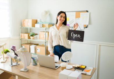 Cheerful woman holding an open sign and looking happy working from home selling jewelry online