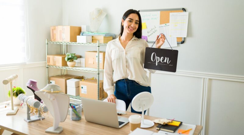 Cheerful woman holding an open sign and looking happy working from home selling jewelry online