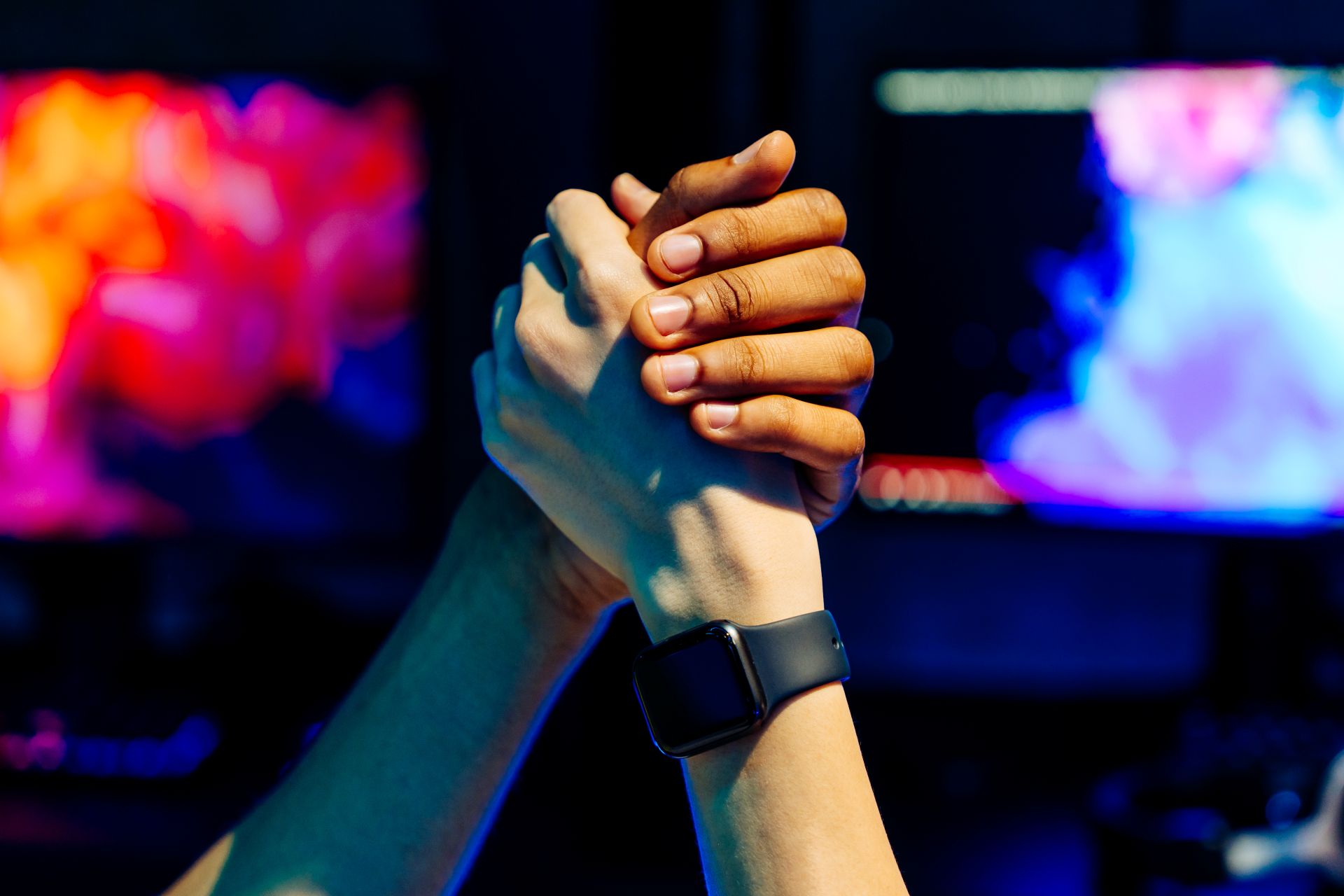 Two gamers clasping hands in front of glowing monitors – symbol of friendship, teamwork, and community in online gaming servers