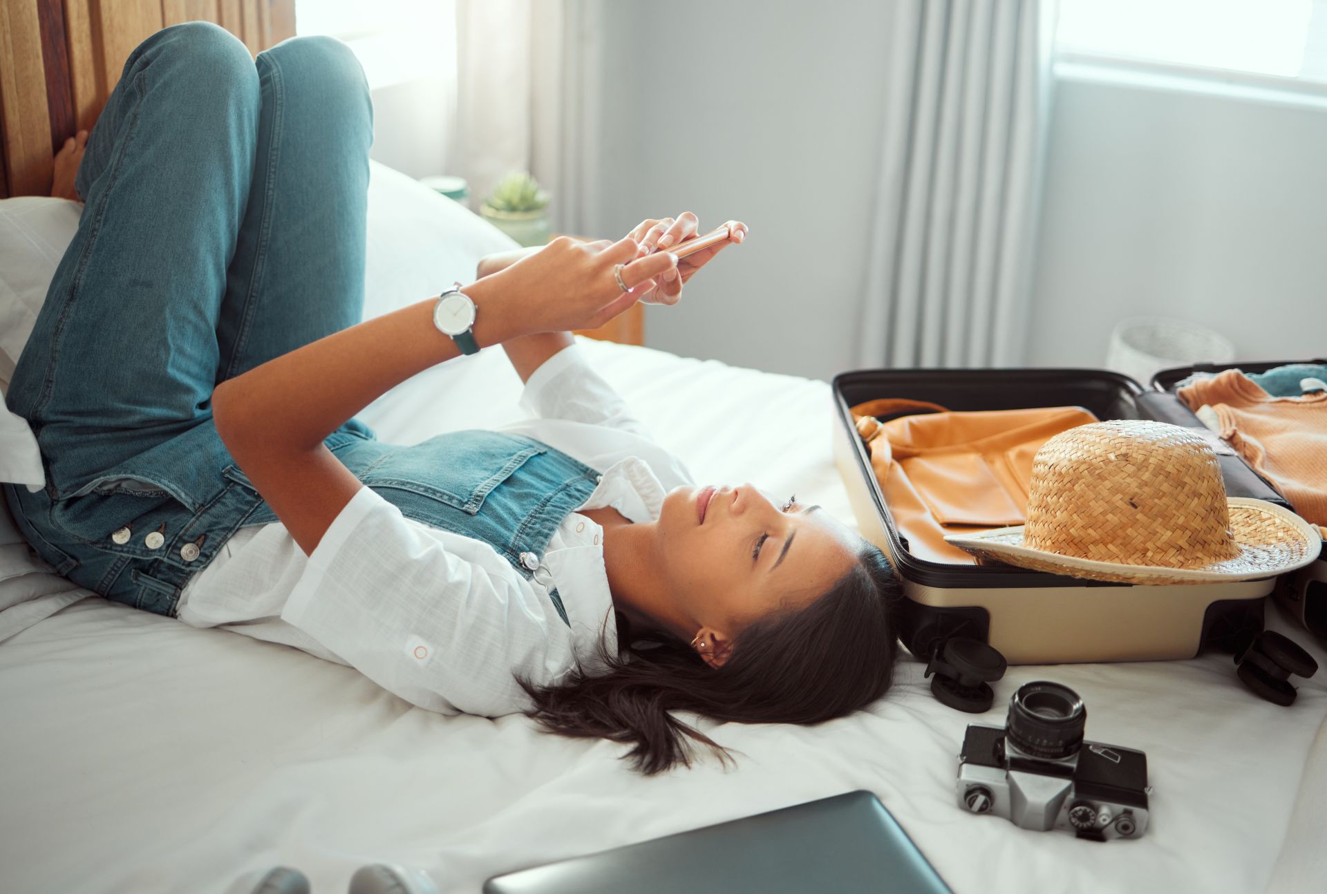 Creator relaxing on bed while checking phone next to an open suitcase, illustrating flexible travel routines supported by an onlyfans agency.